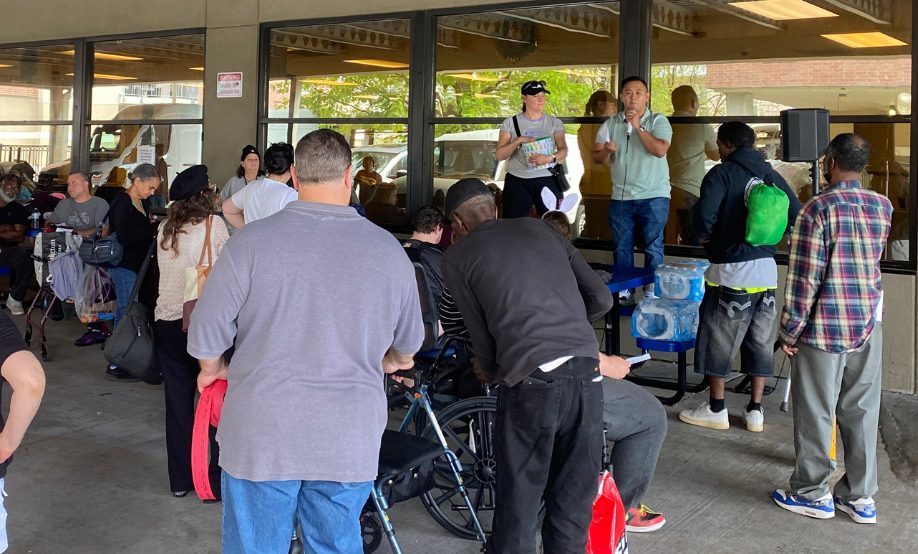 Ace preaching with a microphone to a crowd outside Ozanam Inn